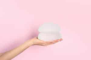 Hand holding breast implants with solid pink background, Denver, CO