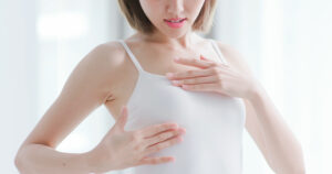 Woman cupping her breast through shirt considering revision after breast reconstruction