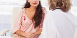 Woman wearing pink breast cancer ribbon in consultation with doctor to prepare for breast reconstruction surgery.