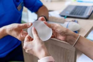 Woman in consultation with doctor holding breast implant to discuss breast reconstruction options of implants vs. fat grafting.