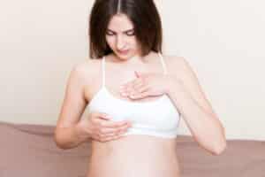Woman in a white bra gently touching her chest, checking for sensation after breast reconstruction.
