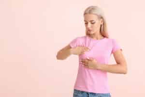 Woman in t-shirt performing breast exam to check for signs of breast cancer
