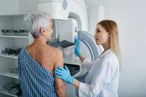 Older woman preparing for a mammogram while a healthcare professional explains breast cancer screening and follow-up care.