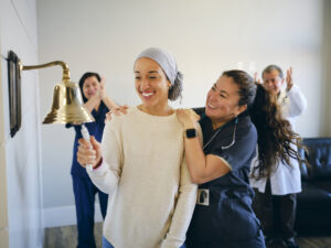 Breast cancer patient ringing a treatment milestone bell with support from her medical care team.