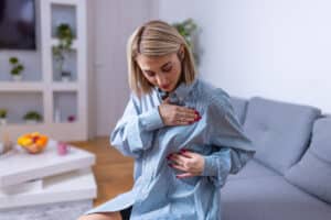 Woman performing a breast self-check at home while considering breast reconstruction options after prior breast surgery.